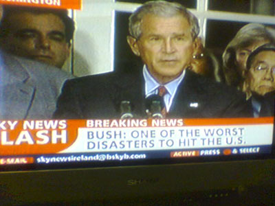 A photograph of a television screen displaying George Bush with a caption stating Bush: One of the worst disasters to hit the US.