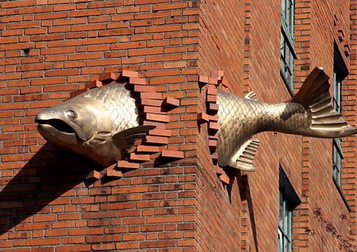 Fish jumping through the corner of a brick building